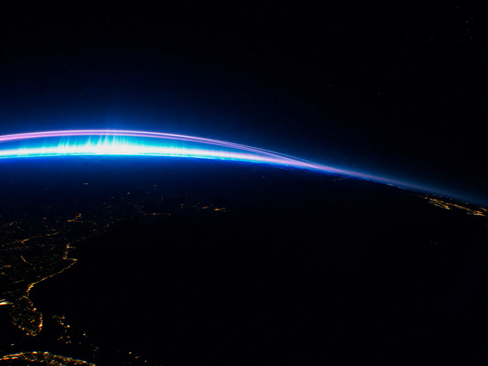 Earth from orbit at night with city lights and a glowing blue atmosphere