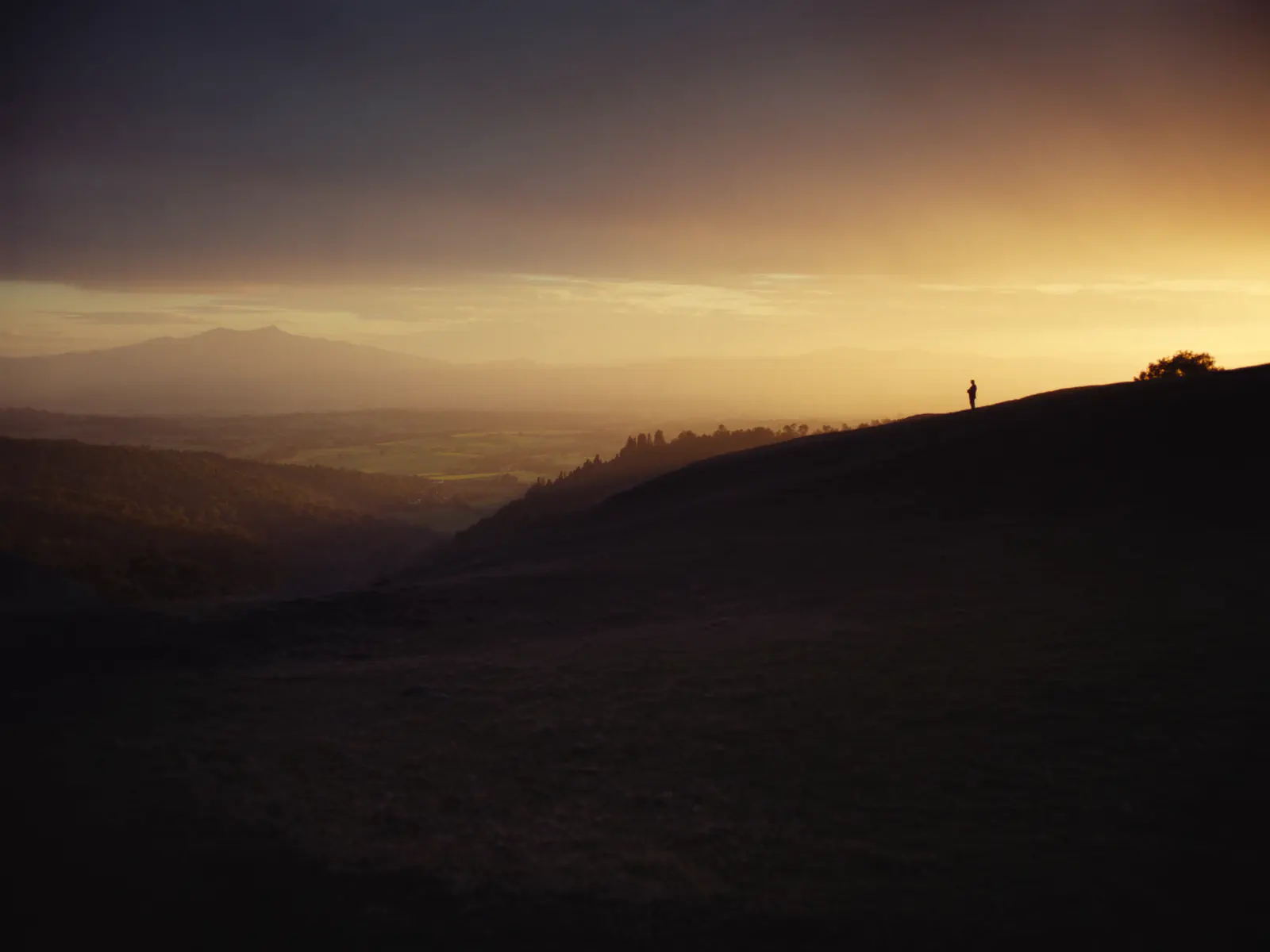 A lone silhouette on a hill overlooking a valley at sunset