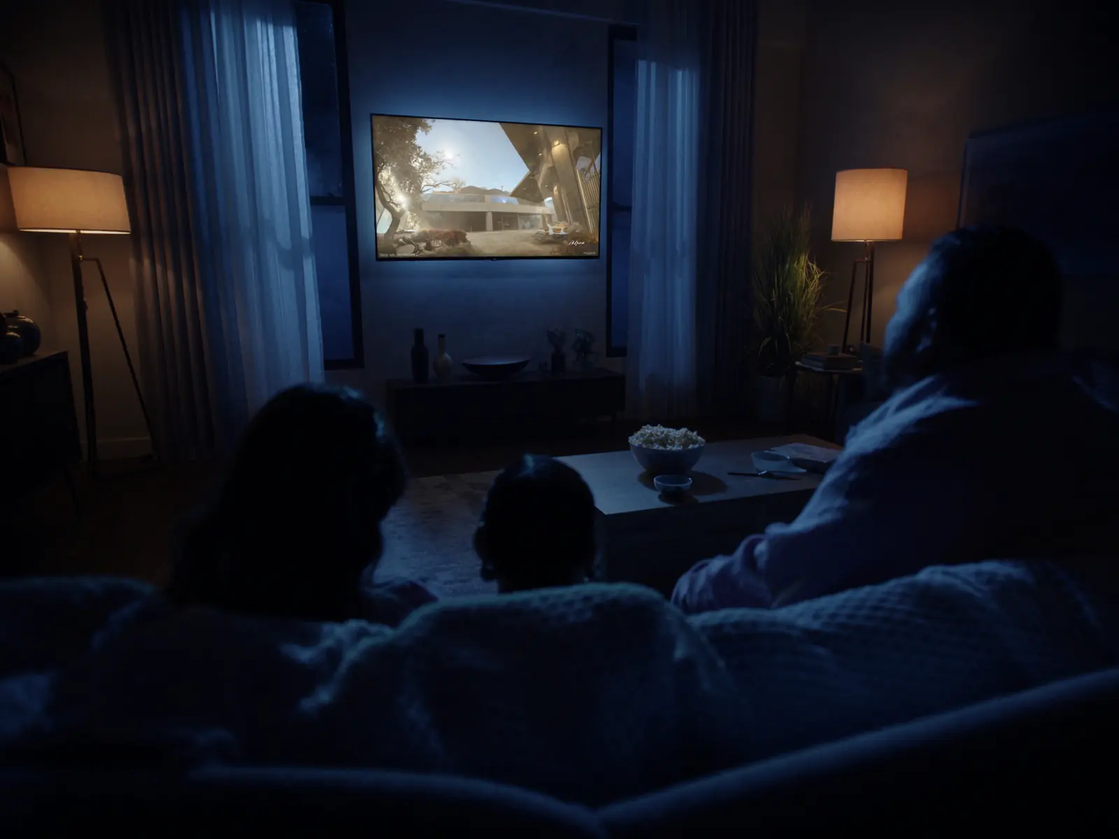 A family on the sofa watching a glowing TV in a cosy living room at night