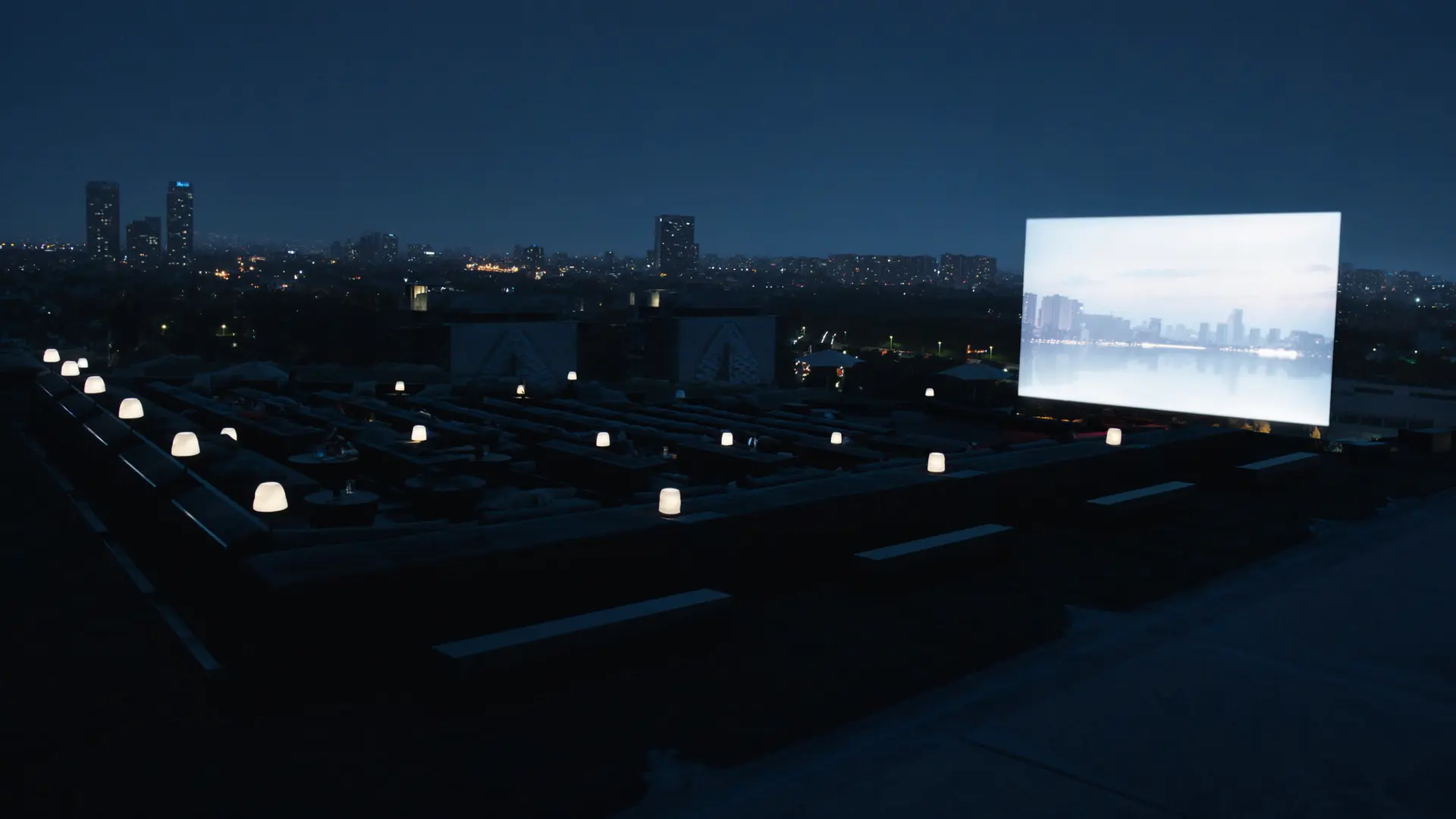 Rooftop cinema screen glowing above a city skyline at night