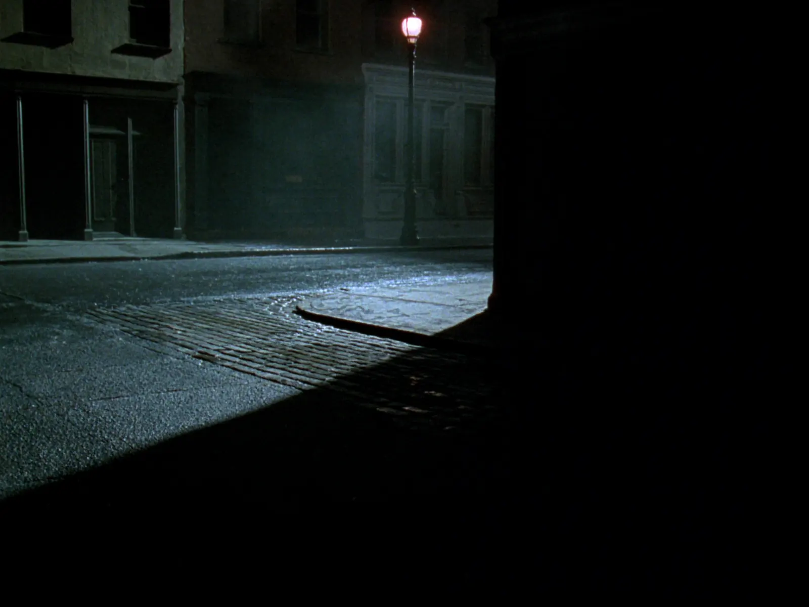 An empty rain-soaked street at night lit by a single street lamp